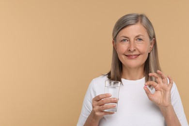 Senior woman with glass of water and pill on beige background. Space for text