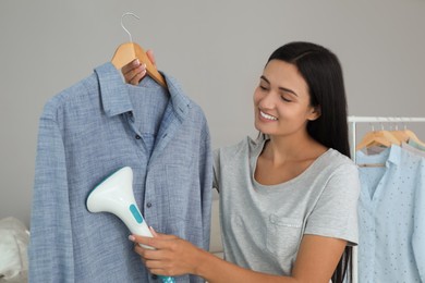 Woman steaming shirt on hanger at home