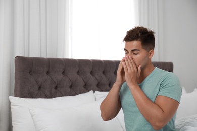 Photo of Young man suffering from allergy in bedroom