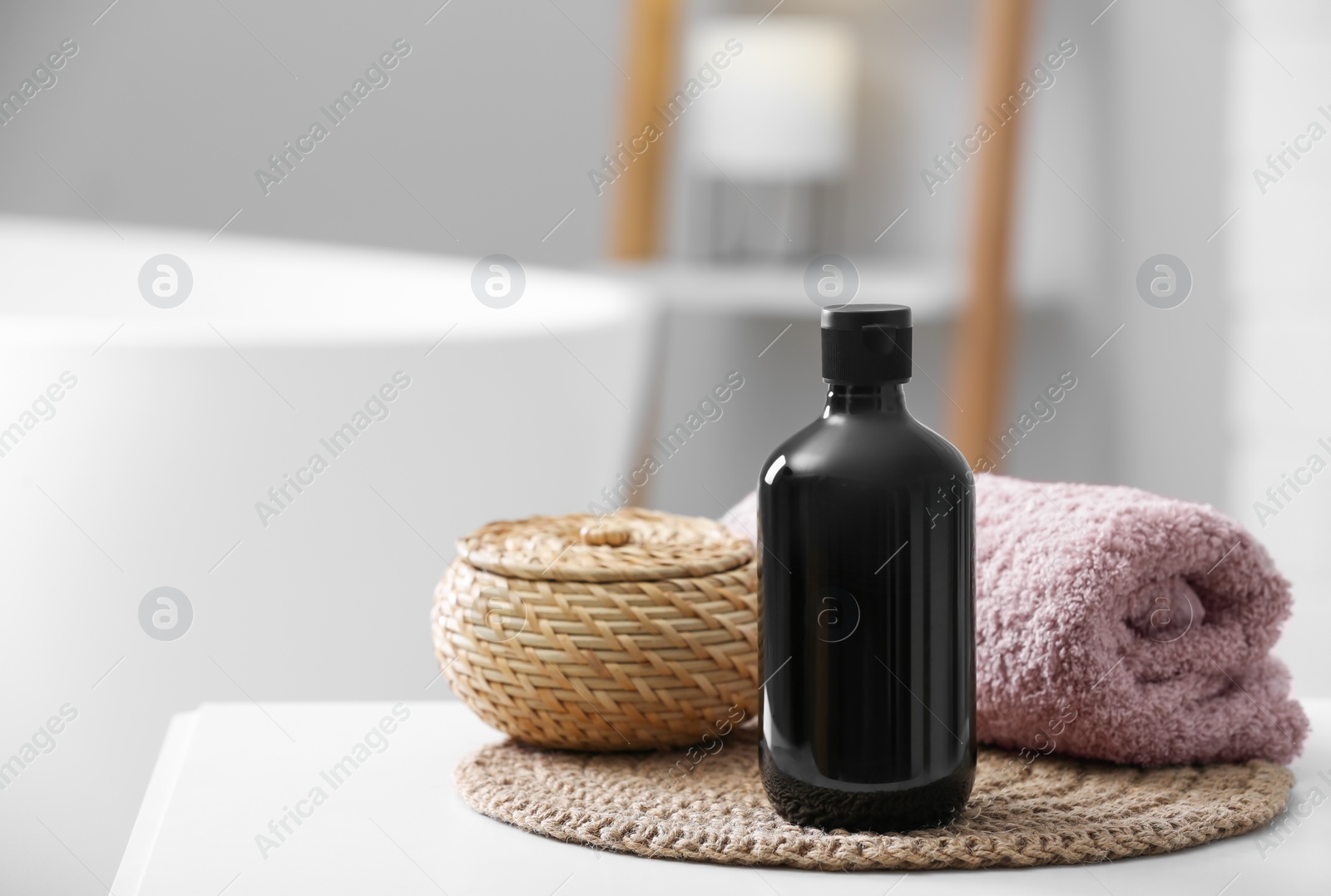 Photo of Bottle of bubble bath, towel and wicker box on white table in bathroom, space for text