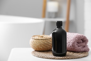 Photo of Bottle of bubble bath, towel and wicker box on white table in bathroom, space for text