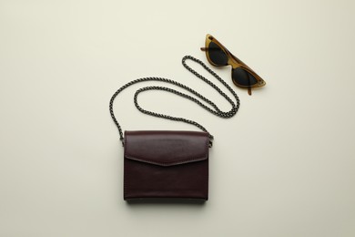 Stylish woman's bag and sunglasses on light  background, flat lay