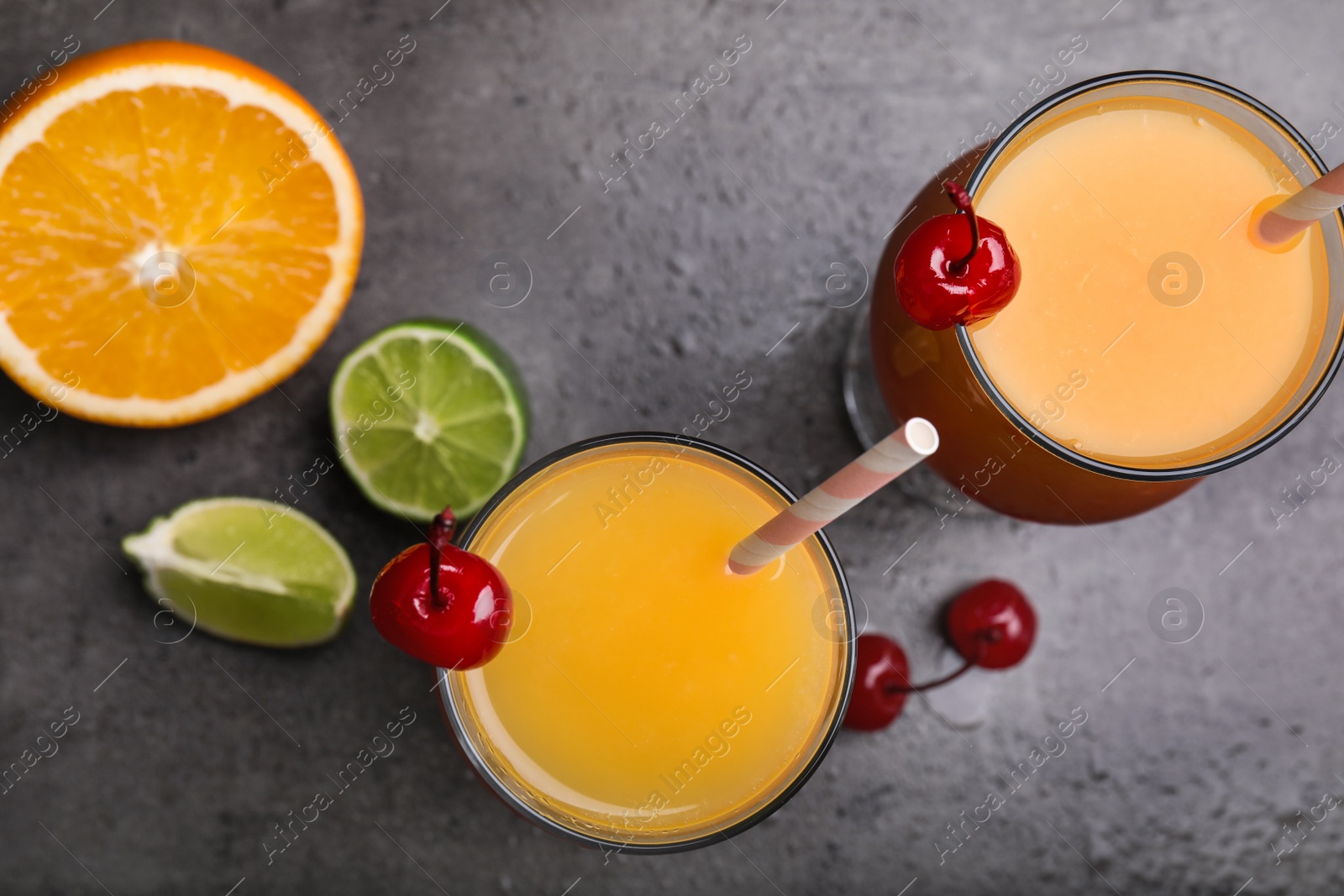 Photo of Fresh alcoholic Tequila Sunrise cocktails on grey table, flat lay