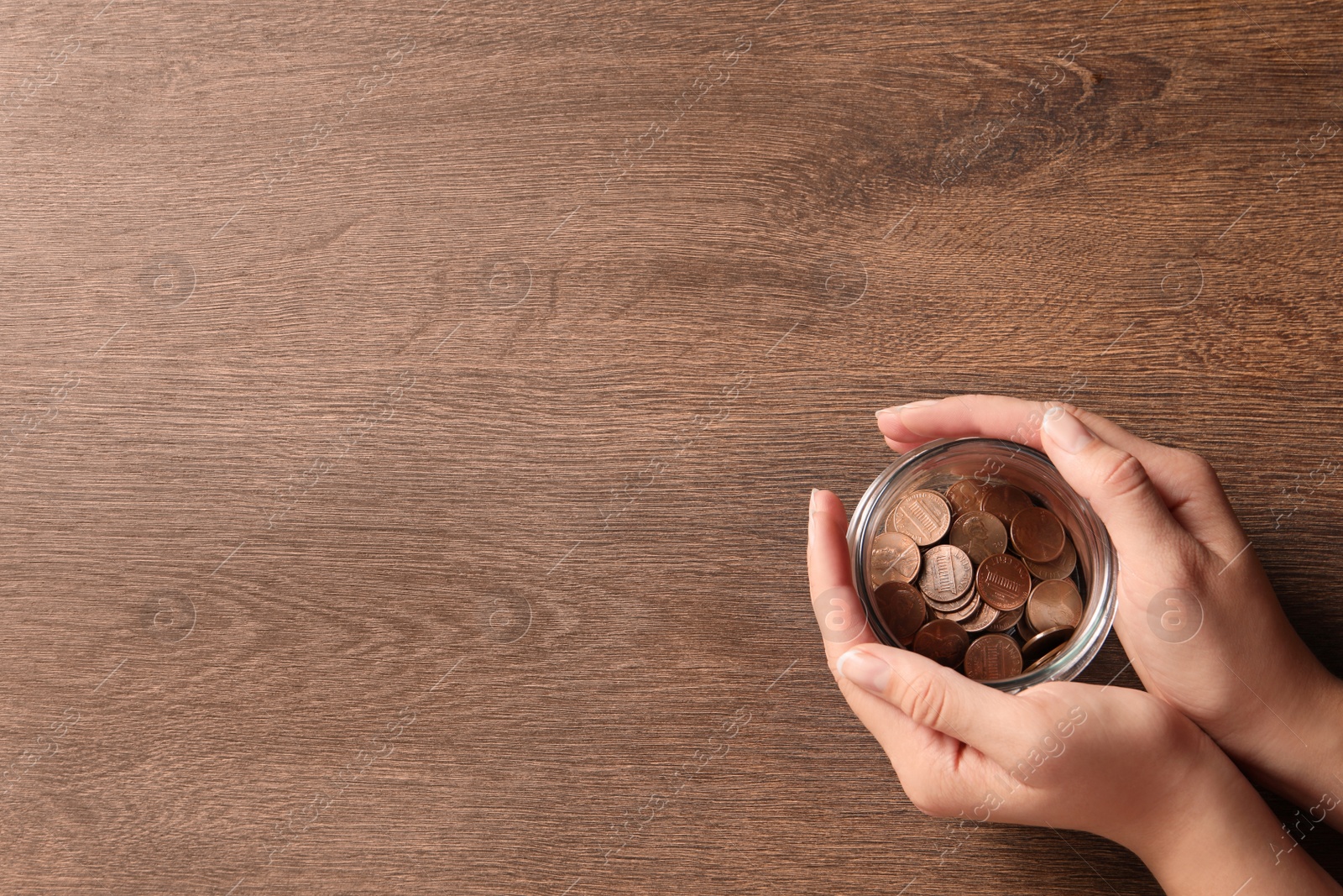 Photo of Woman holding glass jar with coins on wooden table, closeup. Space for text