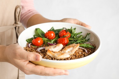 Woman holding bowl of buckwheat porridge with meat and vegetables on light background, closeup