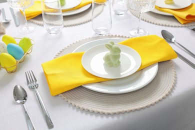 Photo of Festive table setting with cutlery, plate and bunny figure. Easter celebration