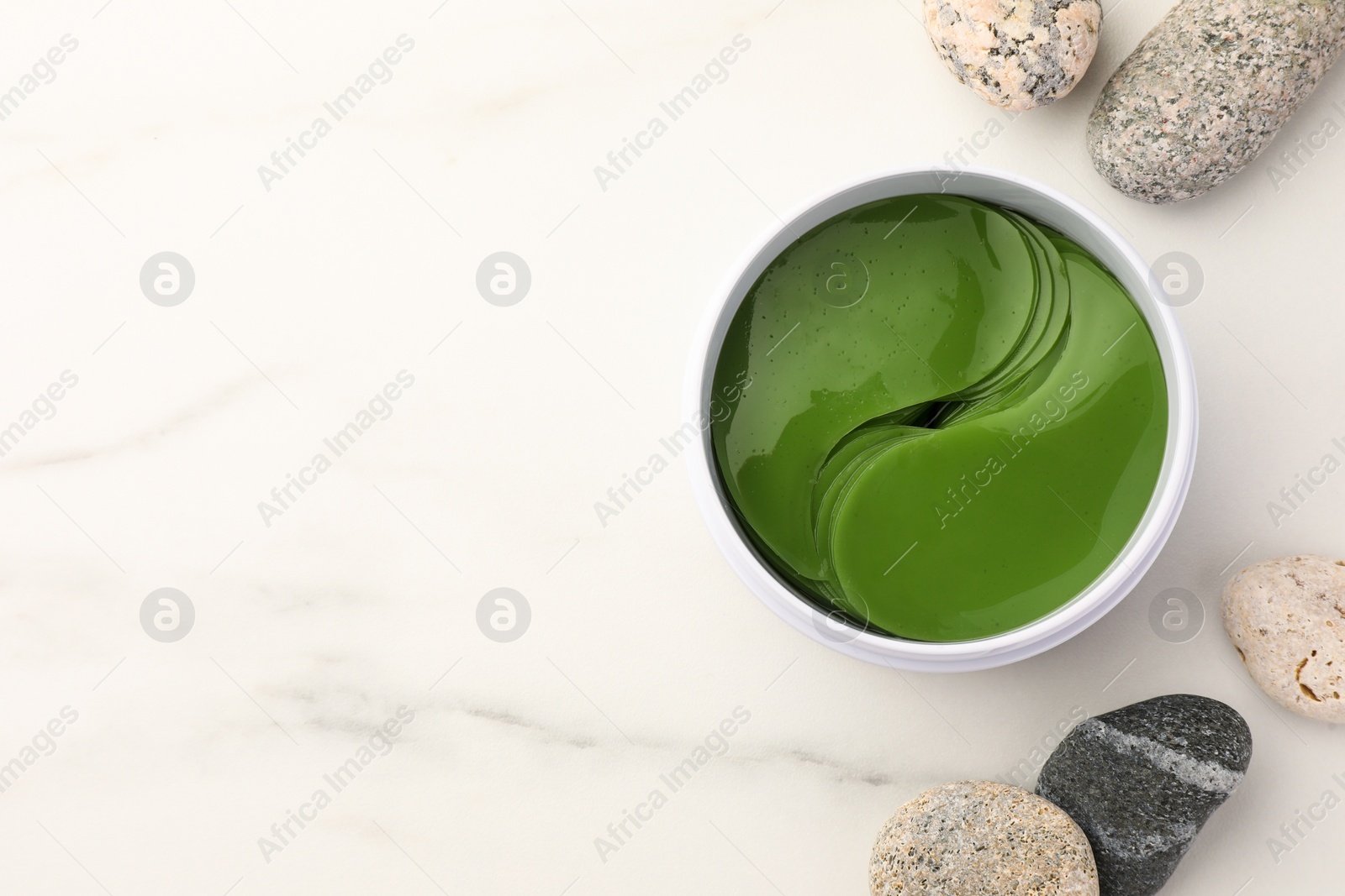 Photo of Jar of under eye patches and stones on white marble table, flat lay with space for text. Cosmetic product