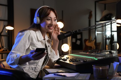 Photo of Woman with smartphone working as radio host in modern studio