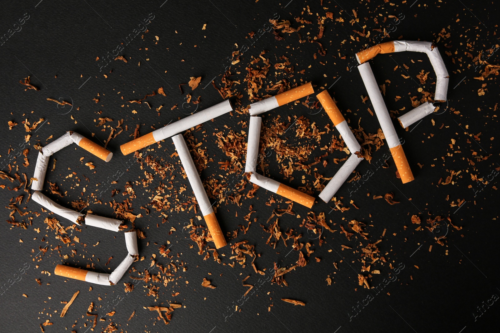 Photo of Word Stop made of broken cigarettes on black background, flat lay. Quitting smoking concept