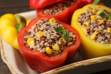 Photo of Quinoa stuffed bell peppers and basil in baking dish on table, closeup