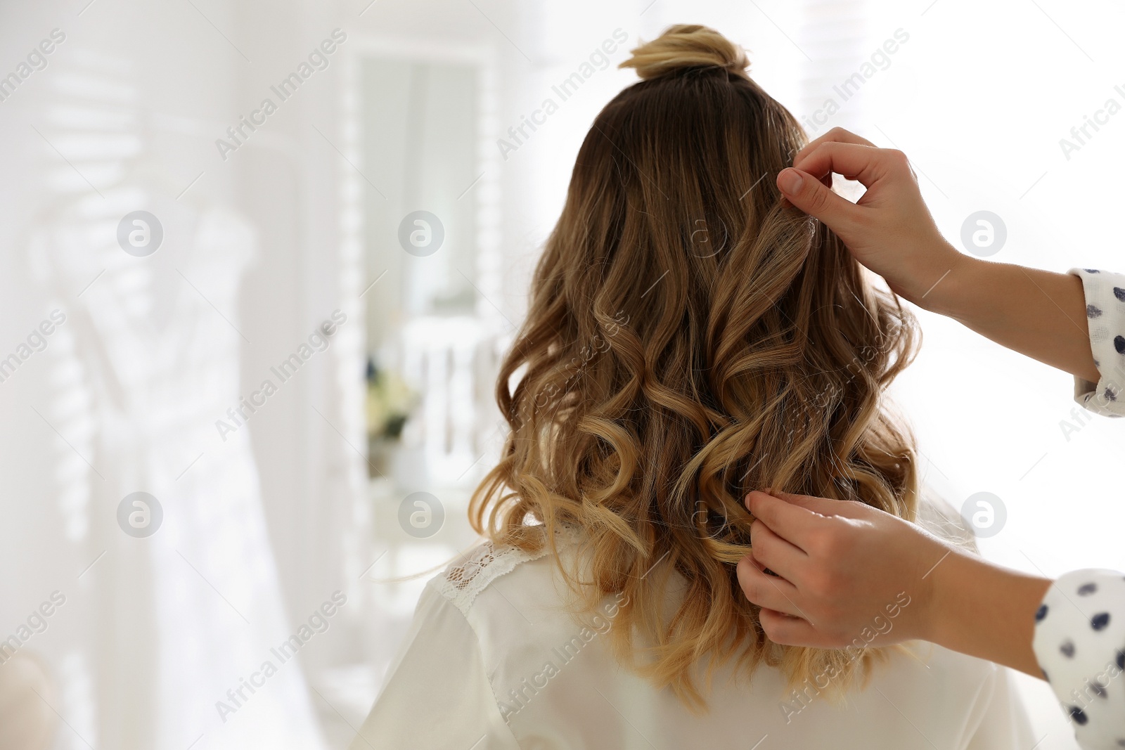 Photo of Professional stylist making wedding hairstyle for bride in salon, back view