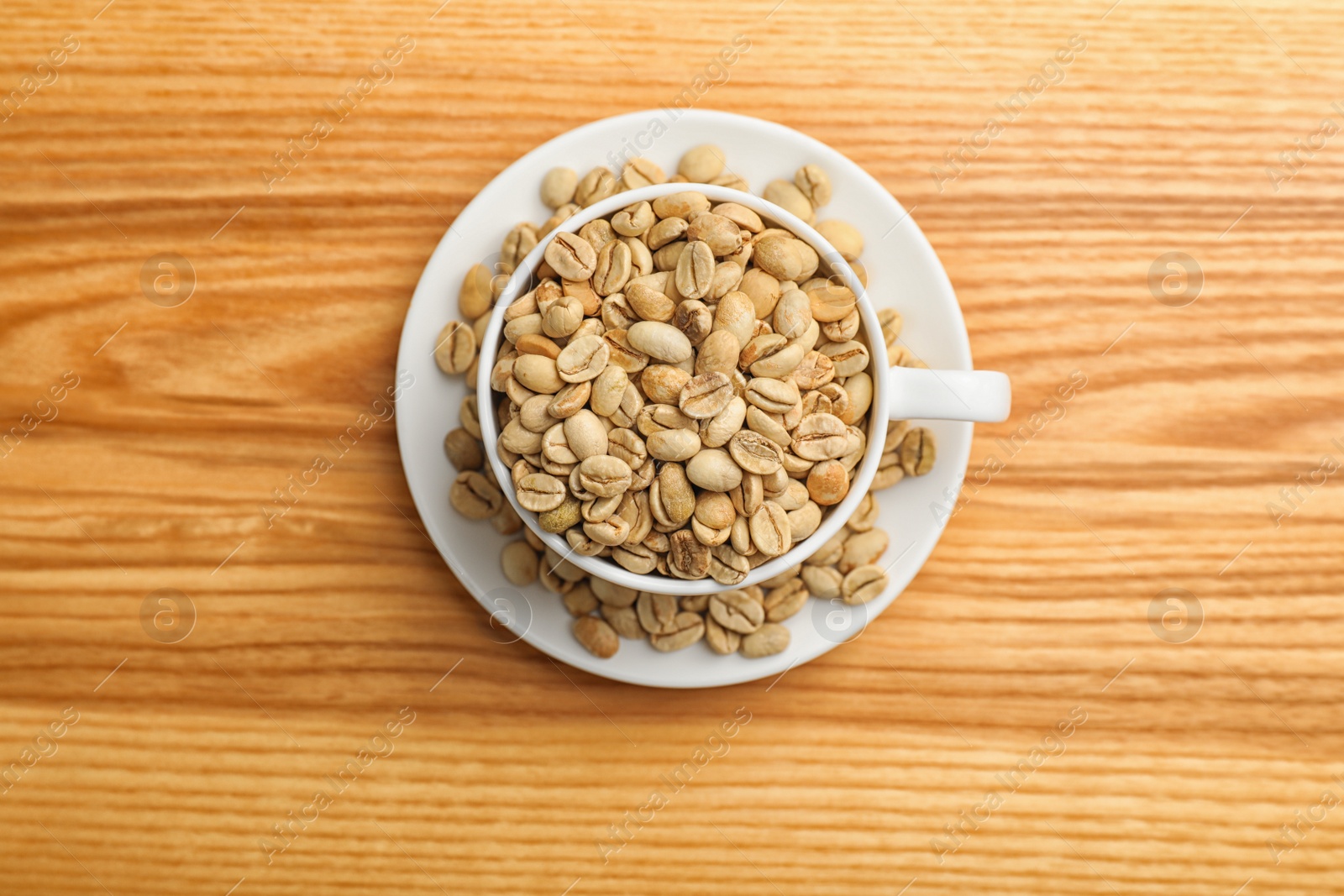 Photo of Cup and saucer with green coffee beans on wooden background, top view