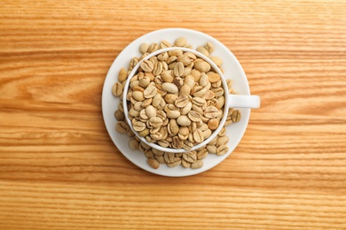 Photo of Cup and saucer with green coffee beans on wooden background, top view