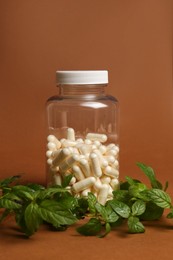 Photo of Transparent medicine bottle and green leaves on brown background