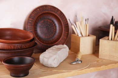 Photo of Set of different crafting tools and clay dishes on wooden rack in workshop