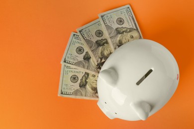 Photo of Ceramic piggy bank and banknotes on orange background, flat lay. Space for text