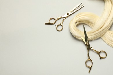 Professional hairdresser scissors with blonde hair strand on light grey background, flat lay. Space for text