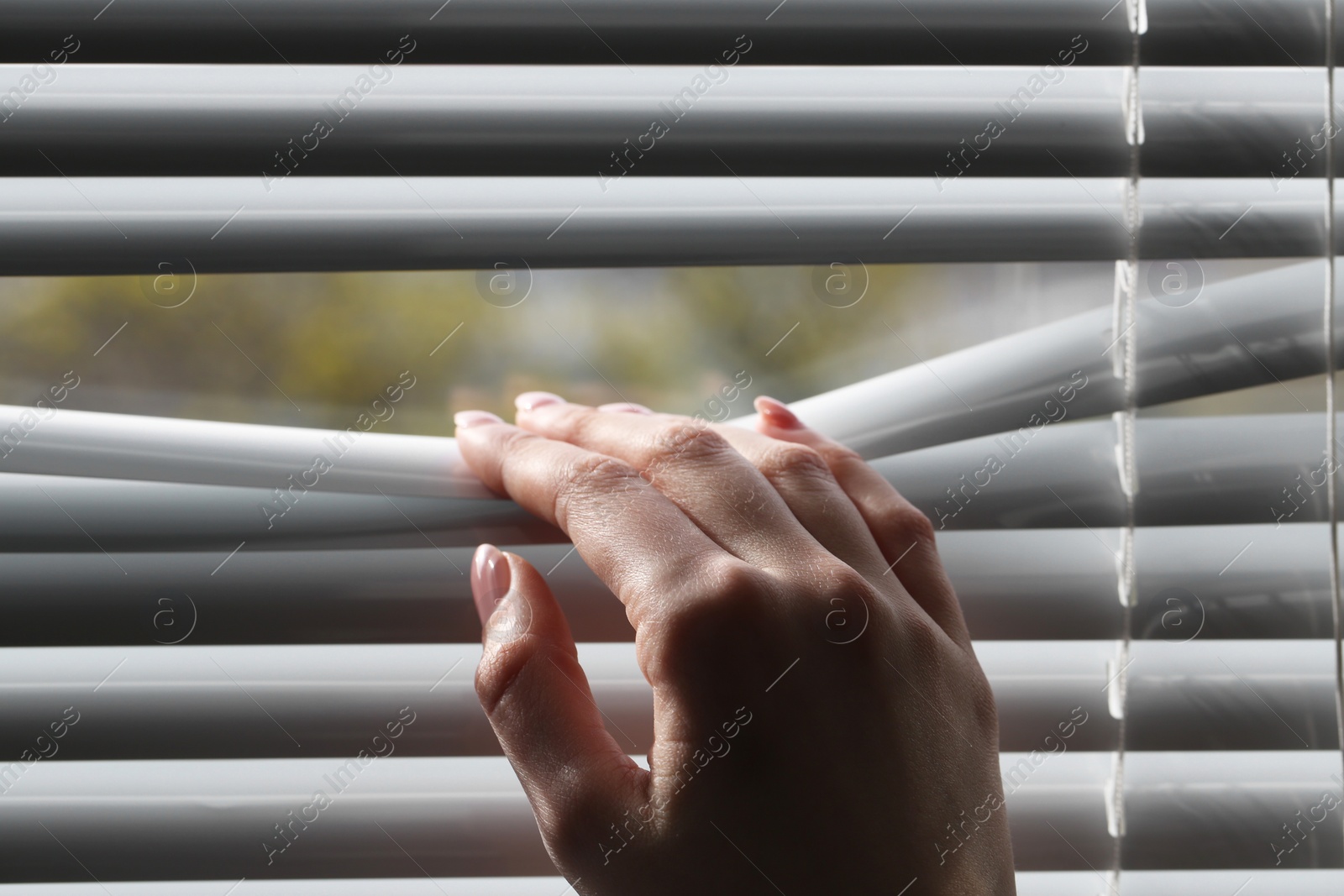 Photo of Woman separating slats of white blinds indoors, closeup