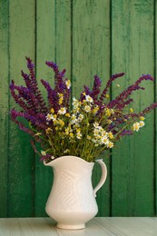 Beautiful bouquet with field flowers in jug on white wooden table