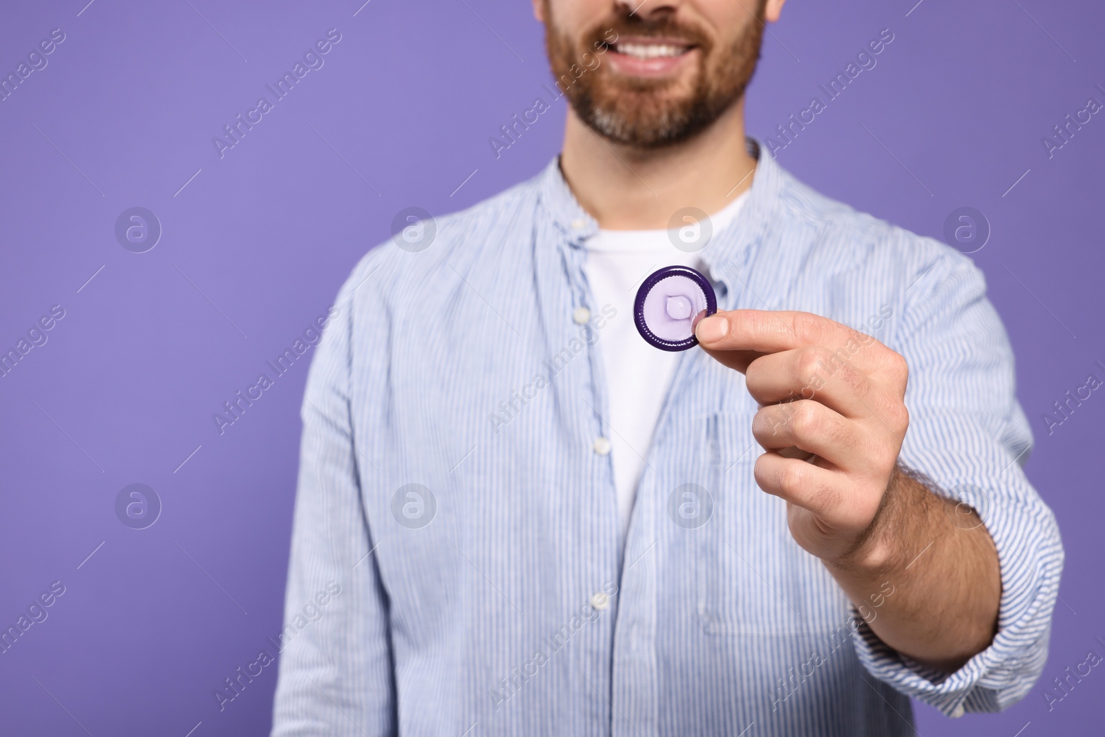 Photo of Man holding condom on purple background, closeup. Safe sex