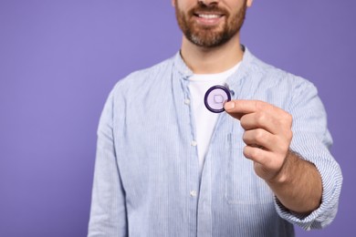 Photo of Man holding condom on purple background, closeup. Safe sex