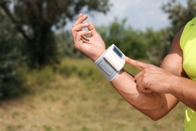 Young man checking pulse with medical device after training in park, closeup. Space for text