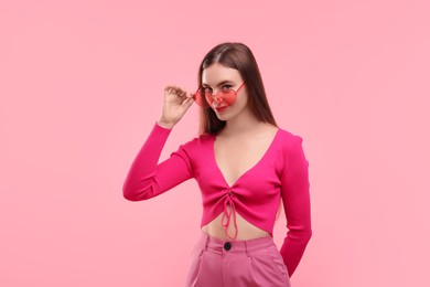 Photo of Beautiful woman in pink clothes and heart shaped sunglasses on color background
