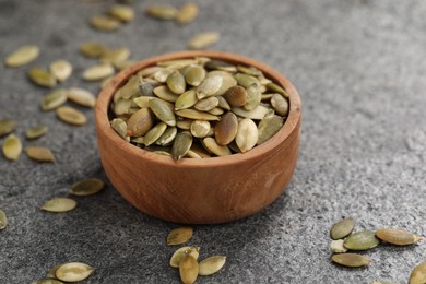 Photo of Wooden bowl with peeled pumpkin seeds on grey table, closeup