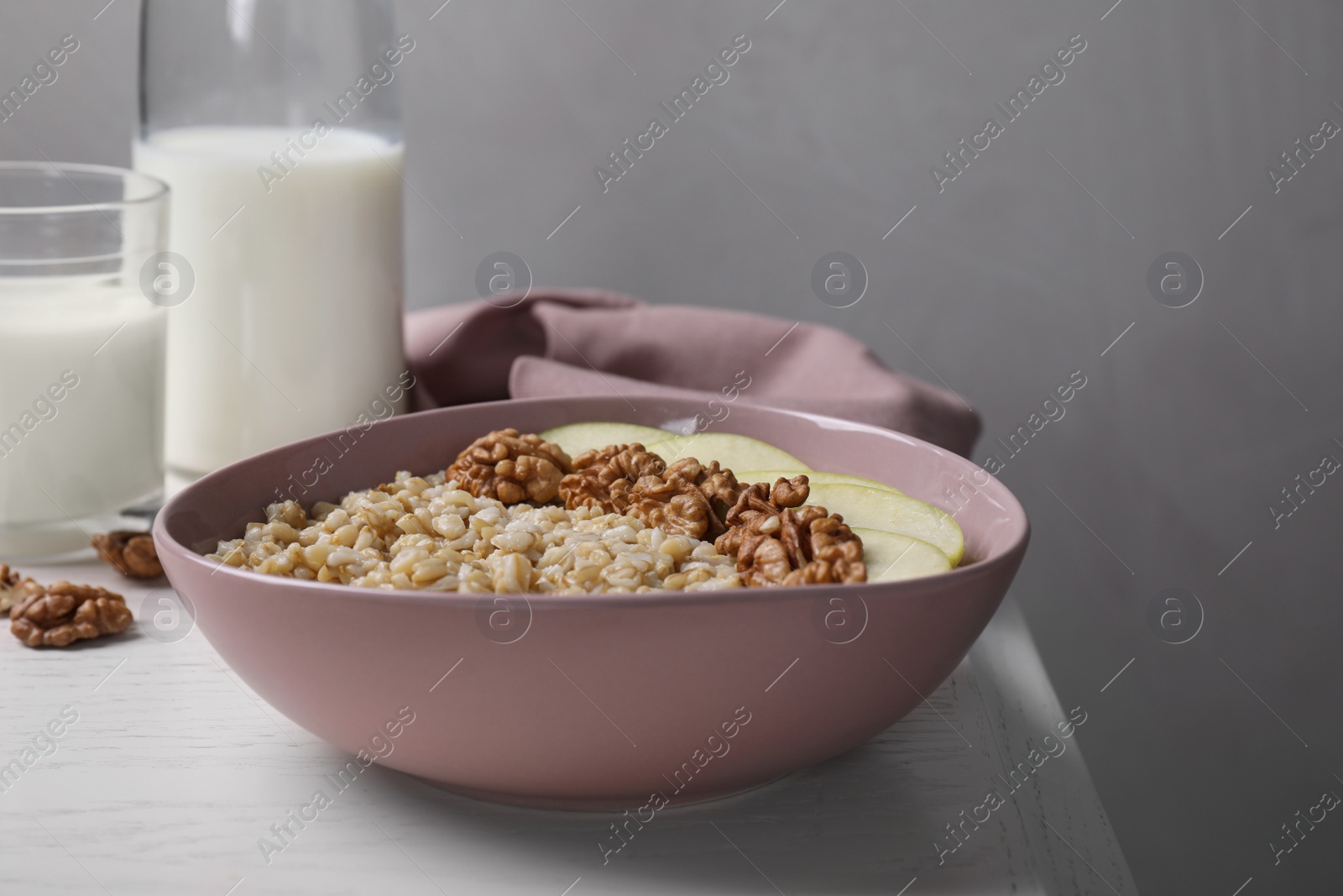 Photo of Tasty oatmeal porridge with walnuts and apple slices on white wooden table