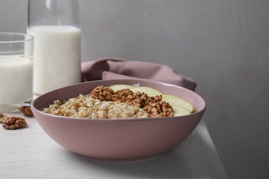 Tasty oatmeal porridge with walnuts and apple slices on white wooden table