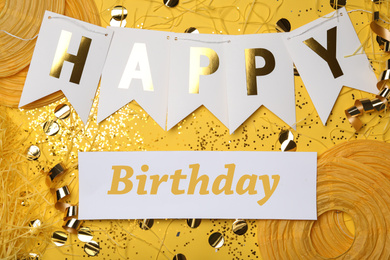 Photo of Flat lay composition with greeting HAPPY BIRTHDAY  and party decor on yellow background