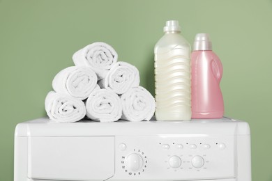 Photo of Washing machine, towels and detergents near green wall