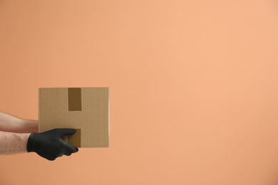 Photo of Courier holding cardboard box on orange background, space for text. Parcel delivery