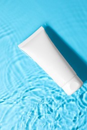 Tube with moisturizing cream in water on light blue background, top view