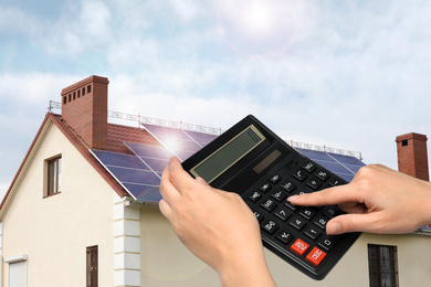 Woman using calculator against house with installed solar panels. Renewable energy and money saving