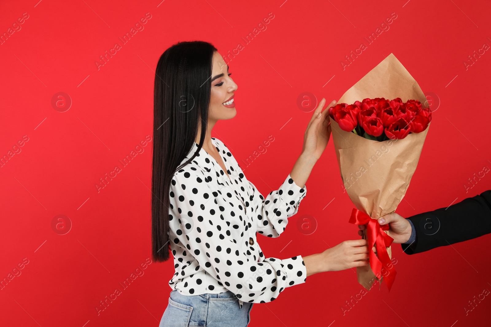 Photo of Happy woman receiving tulip bouquet from man on red background. 8th of March celebration