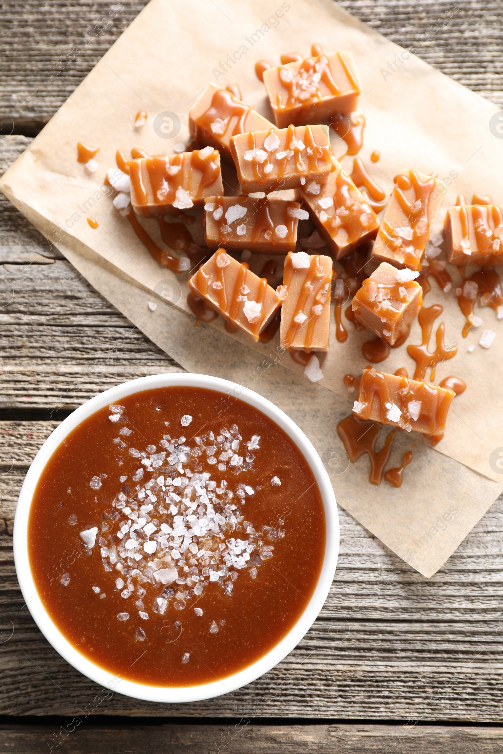 Photo of Caramel sauce with sea salt and yummy candies on wooden table, flat lay