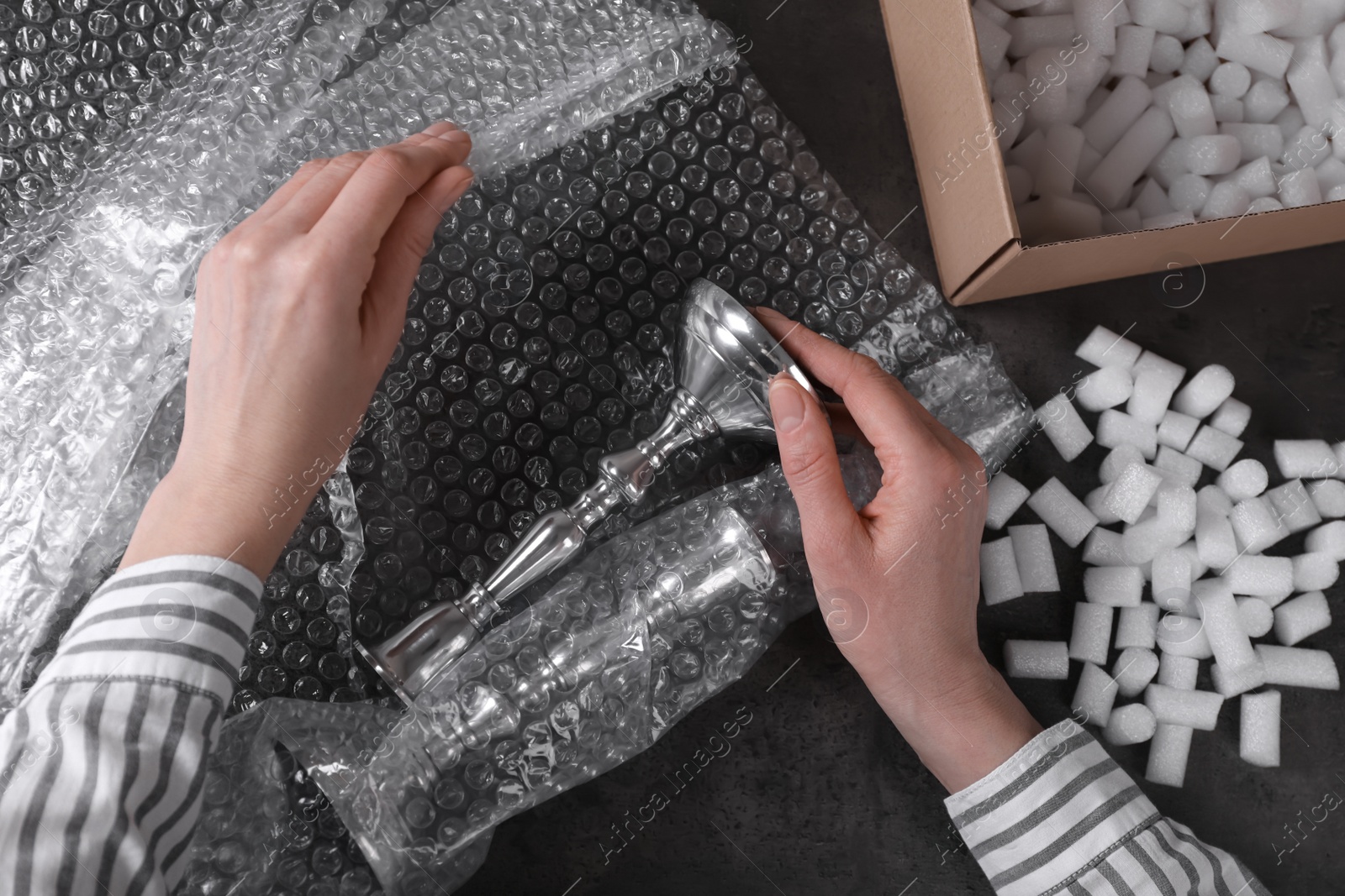 Photo of Woman covering silver candlesticks with bubble wrap at dark grey table, closeup