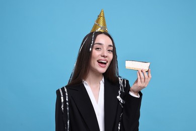 Woman in party hat eating piece of tasty cake on light blue background