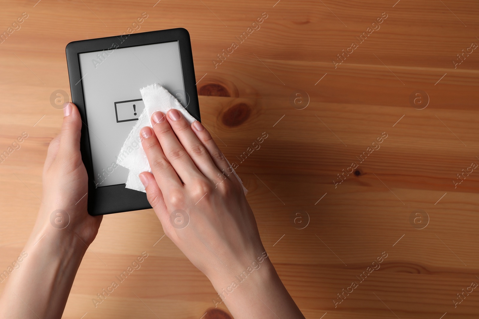 Photo of Woman wiping smartphone with paper at wooden table, top view