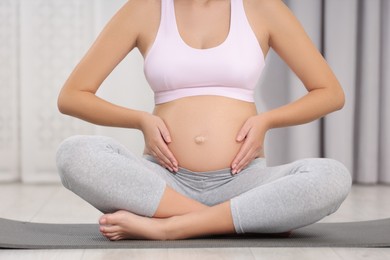 Pregnant woman sitting on yoga mat indoors, closeup