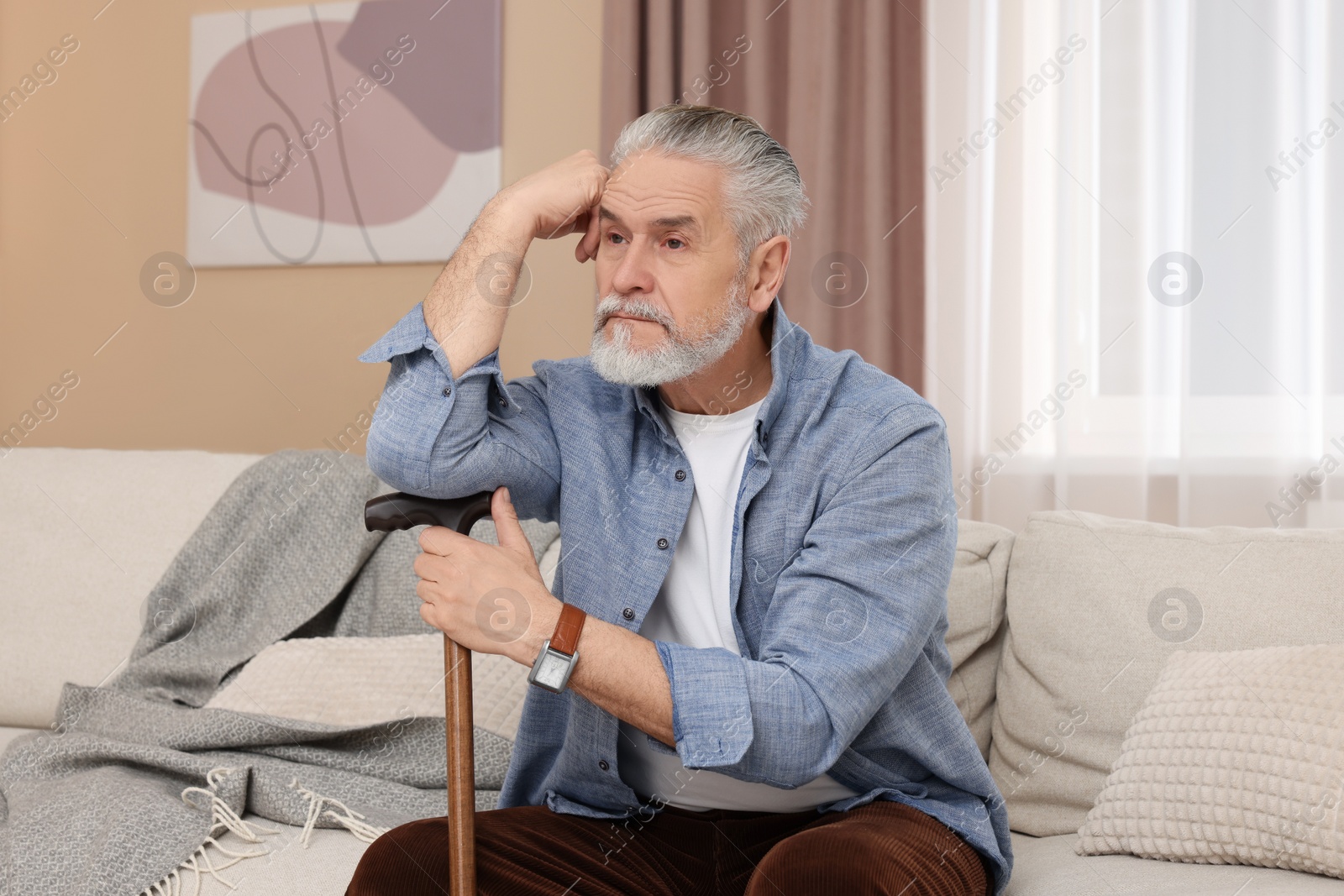 Photo of Senior man with walking cane sitting on sofa at home