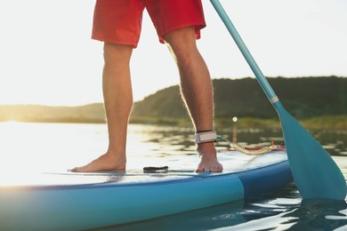 Photo of Man paddle boarding on SUP board in river at sunset, closeup