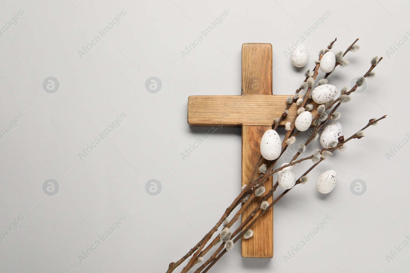 Photo of Wooden cross, painted Easter eggs and willow branches on light grey background, top view. Space for text