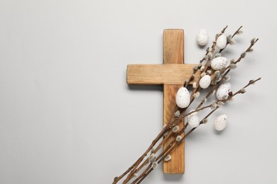 Wooden cross, painted Easter eggs and willow branches on light grey background, top view. Space for text