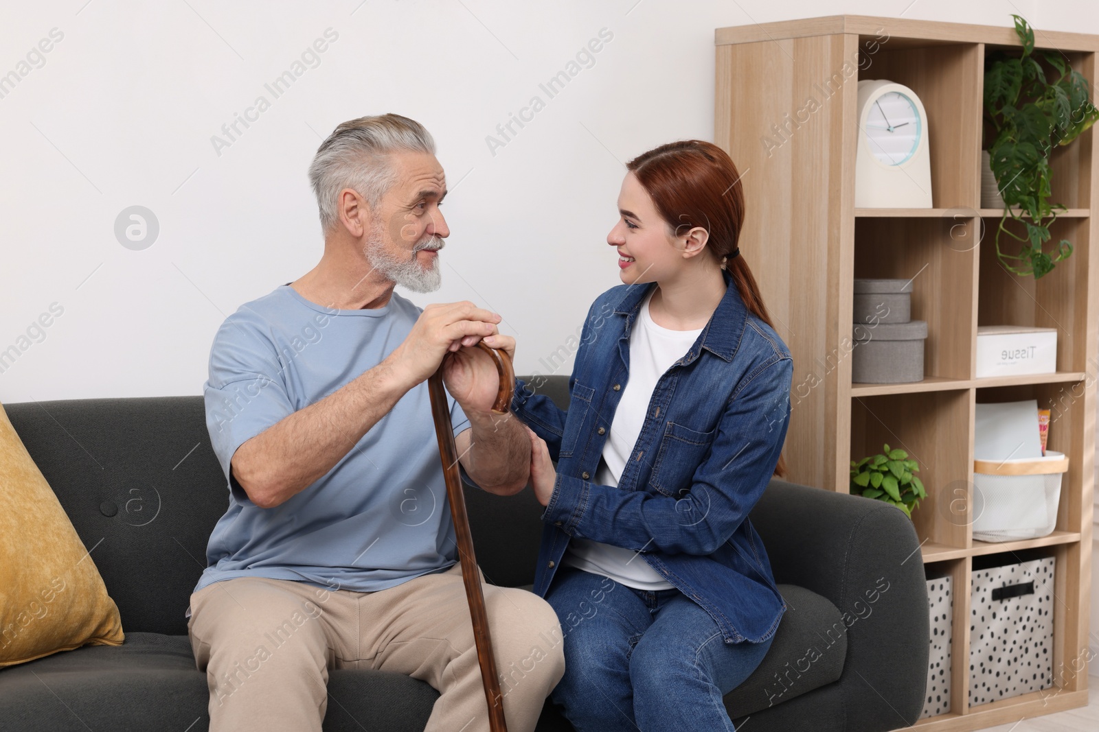 Photo of Caregiver and senior man with walking cane on sofa at home