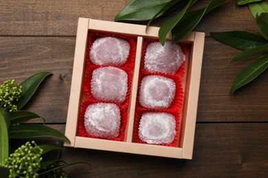 Photo of Box of delicious mochi and leaves on wooden table, flat lay. Traditional Japanese dessert