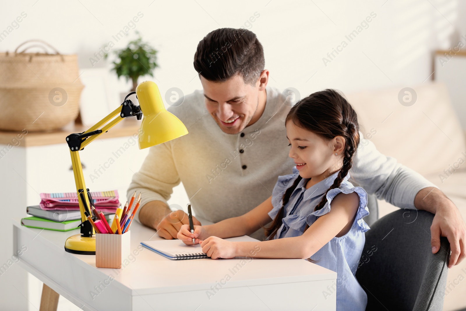 Photo of Man helping his daughter with homework at table indoors