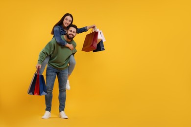 Photo of Happy couple with shopping bags on orange background. Space for text
