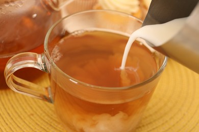 Photo of Pouring milk in tea at table, closeup